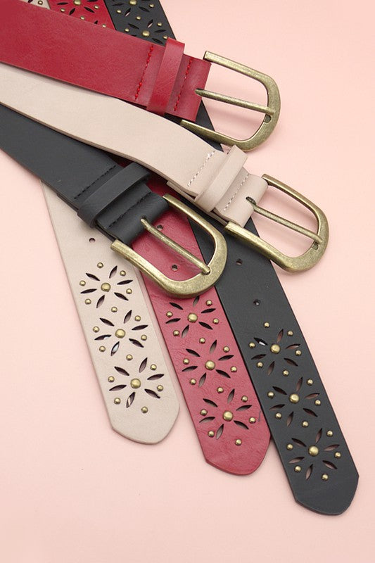 Four leather belts with decorative studs on a pink background