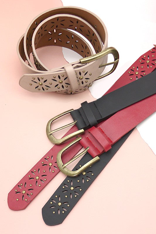 Three leather belts with floral cut-out designs and gold buckles on a light pink background.