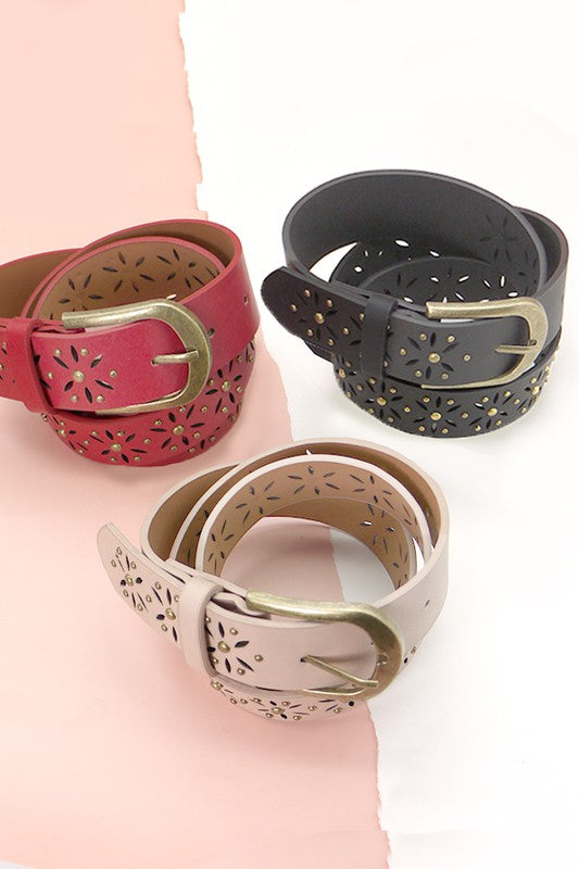 Three leather belts with cut-out designs and gold buckles on a pink surface.
