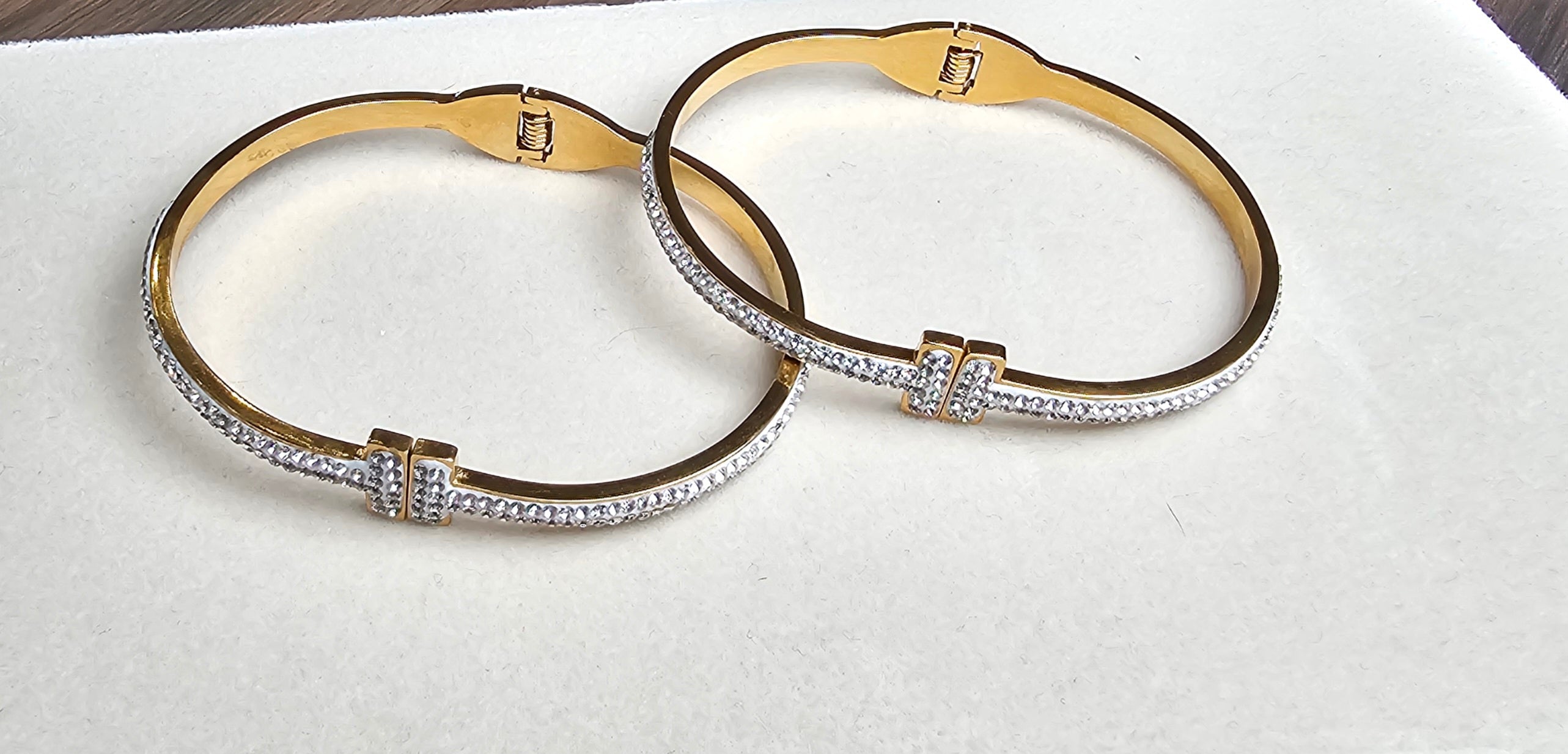 Two gold bangles with diamond accents on a white surface