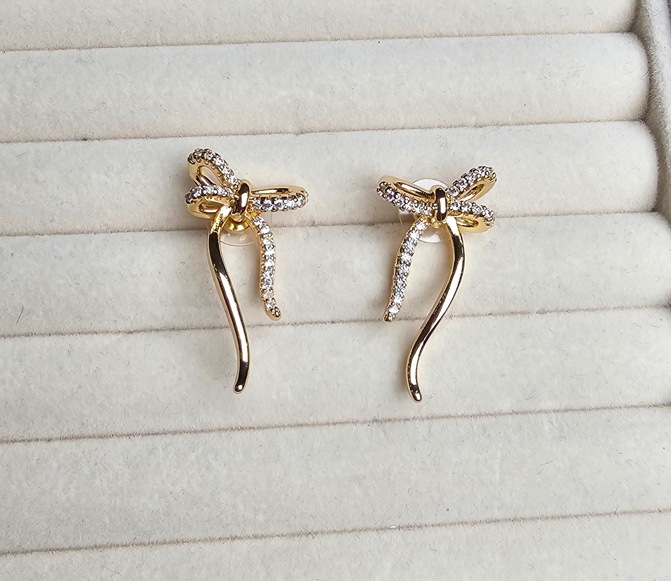 Gold bow-shaped earrings with rhinestones on a light gray surface