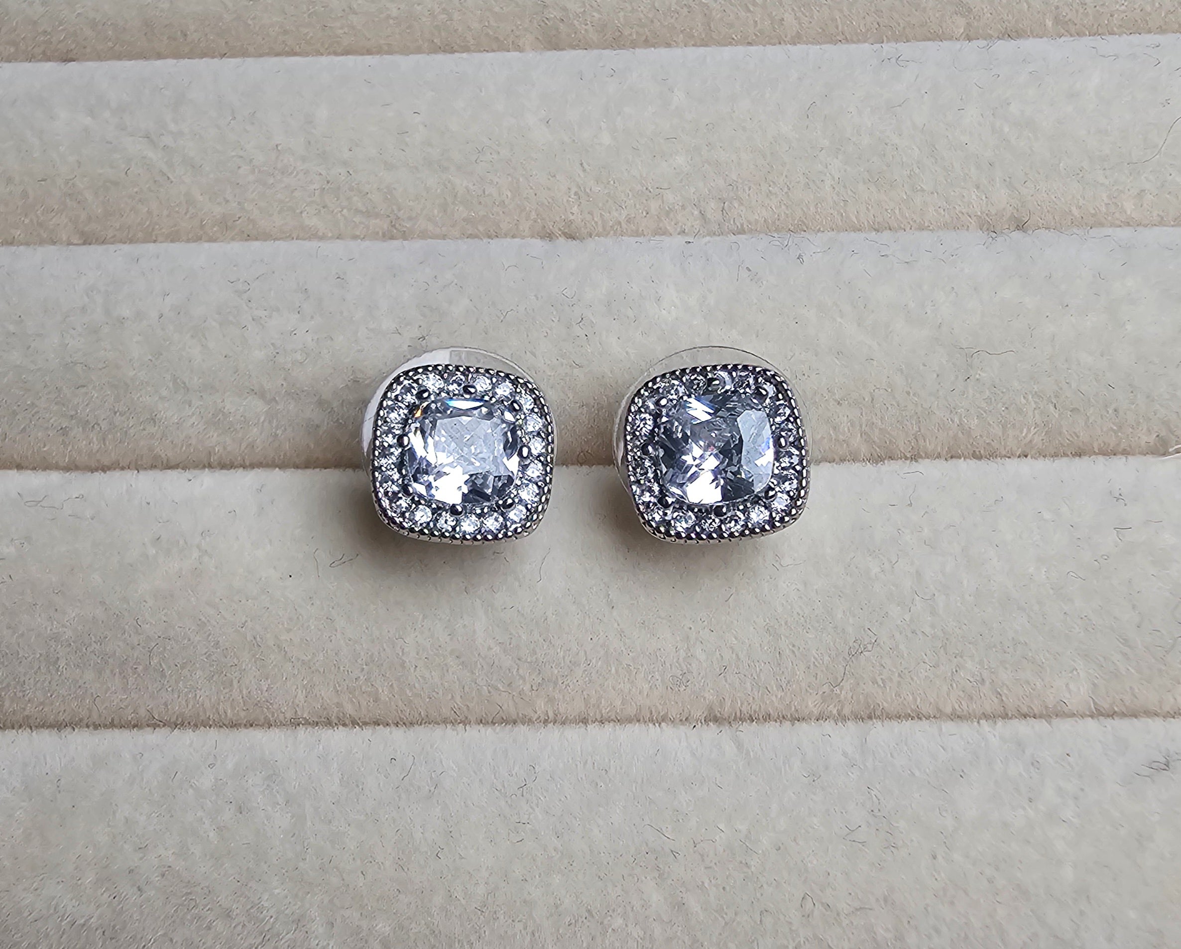Silver square earrings with clear gemstones on a beige surface