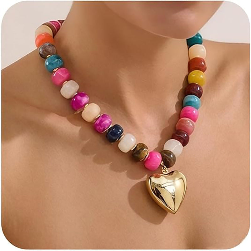Colorful beaded necklace with a gold heart pendant on a person's neck.