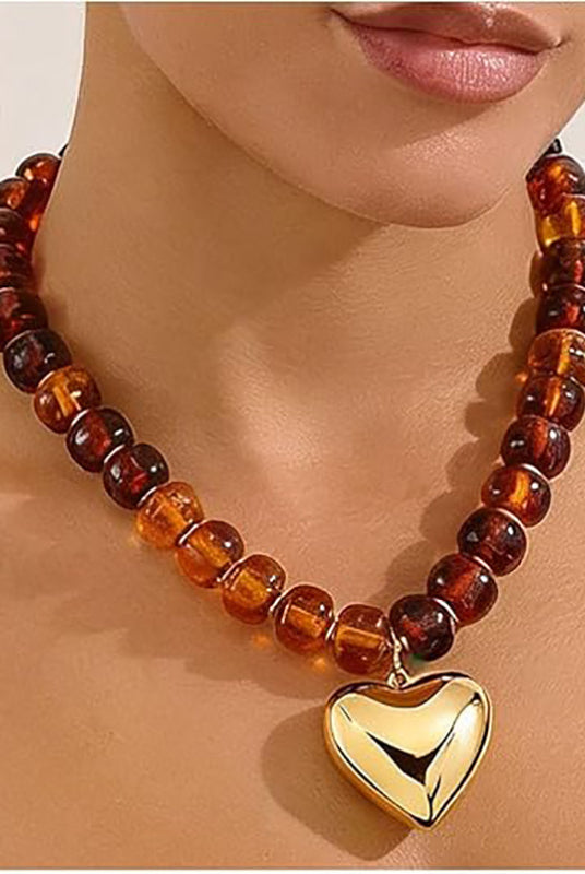 Necklace with amber beads and a gold heart pendant on a person's neck.