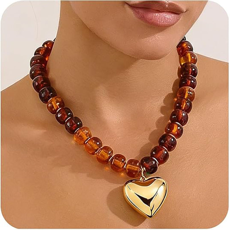 Necklace with amber beads and a gold heart pendant on a person's neck.