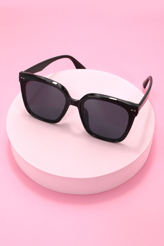Black sunglasses on a white stand against a pink background