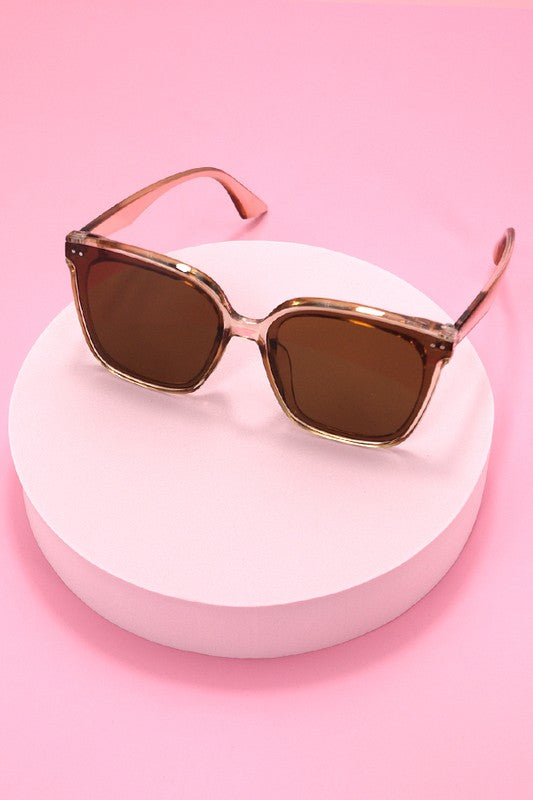 Sunglasses with brown lenses and gold frames on a pink background