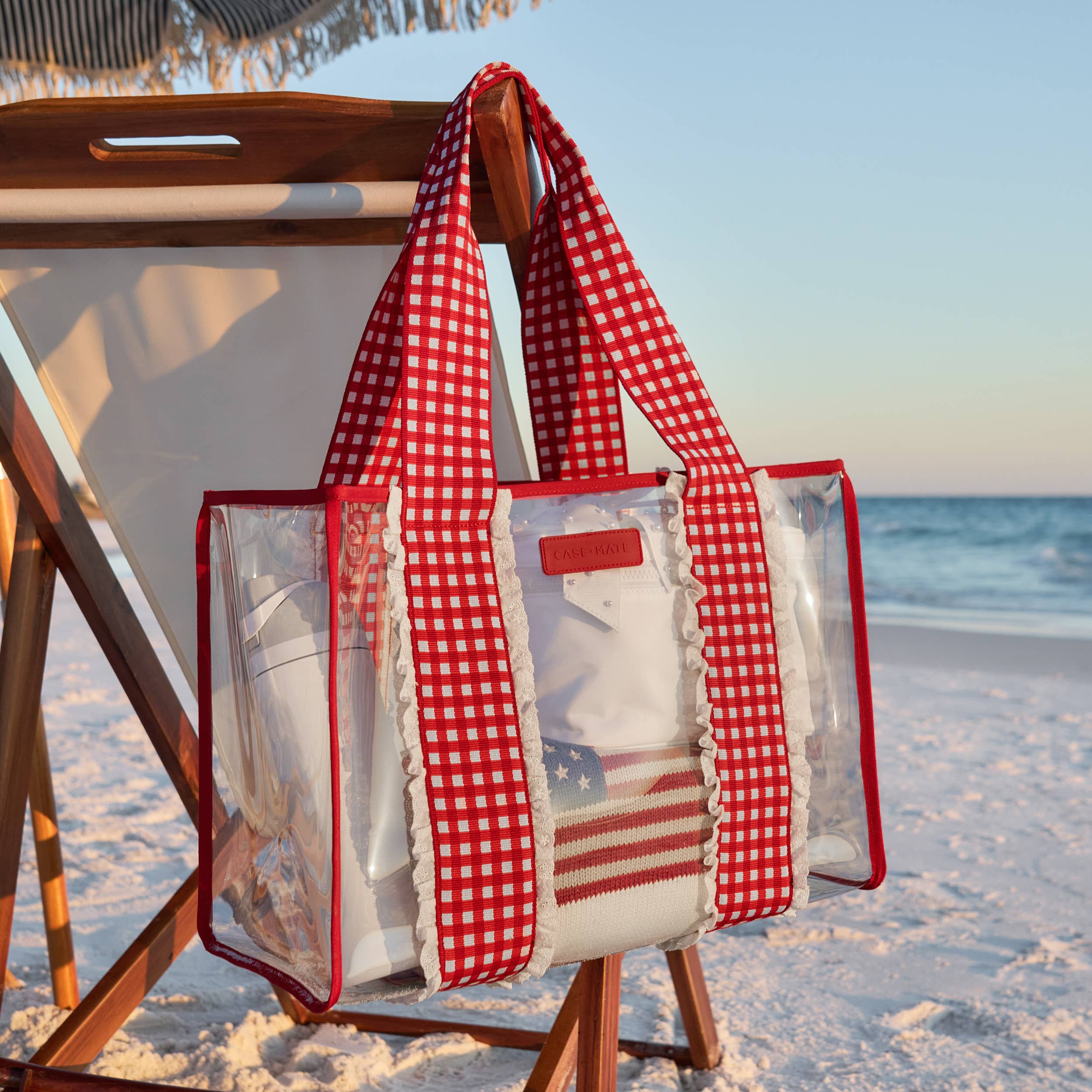 Clear beach bag with red checkered cover on a wooden chair at the beach