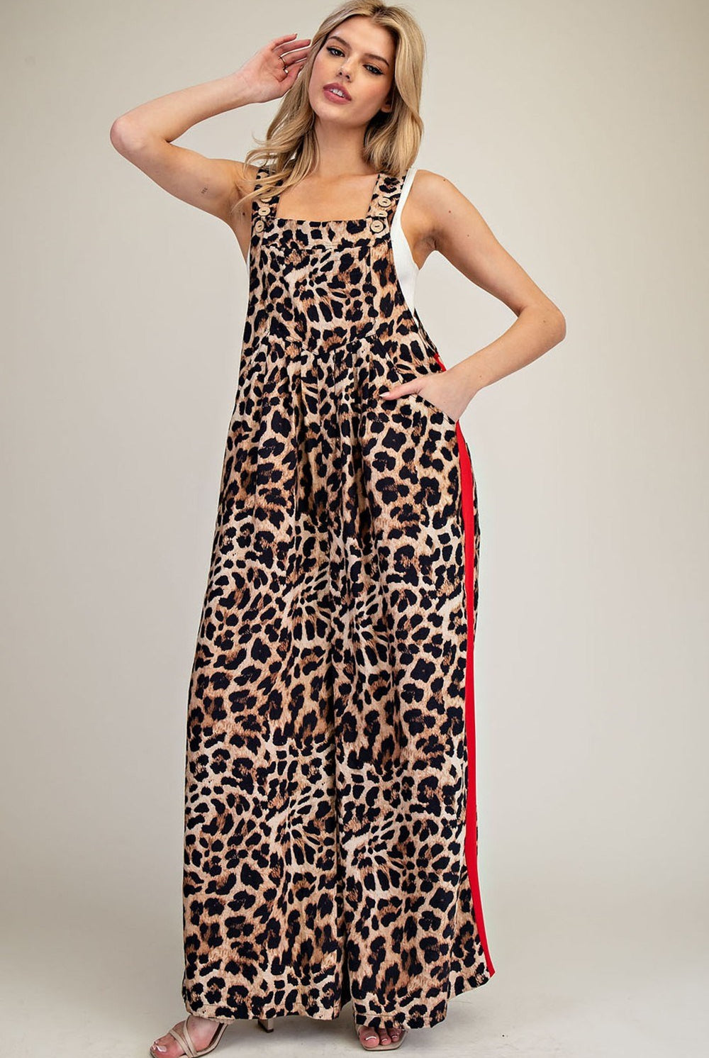 A woman modeling a sleeveless leopard-print maxi dress with a red side stripe, photographed against a plain light beige studio background.