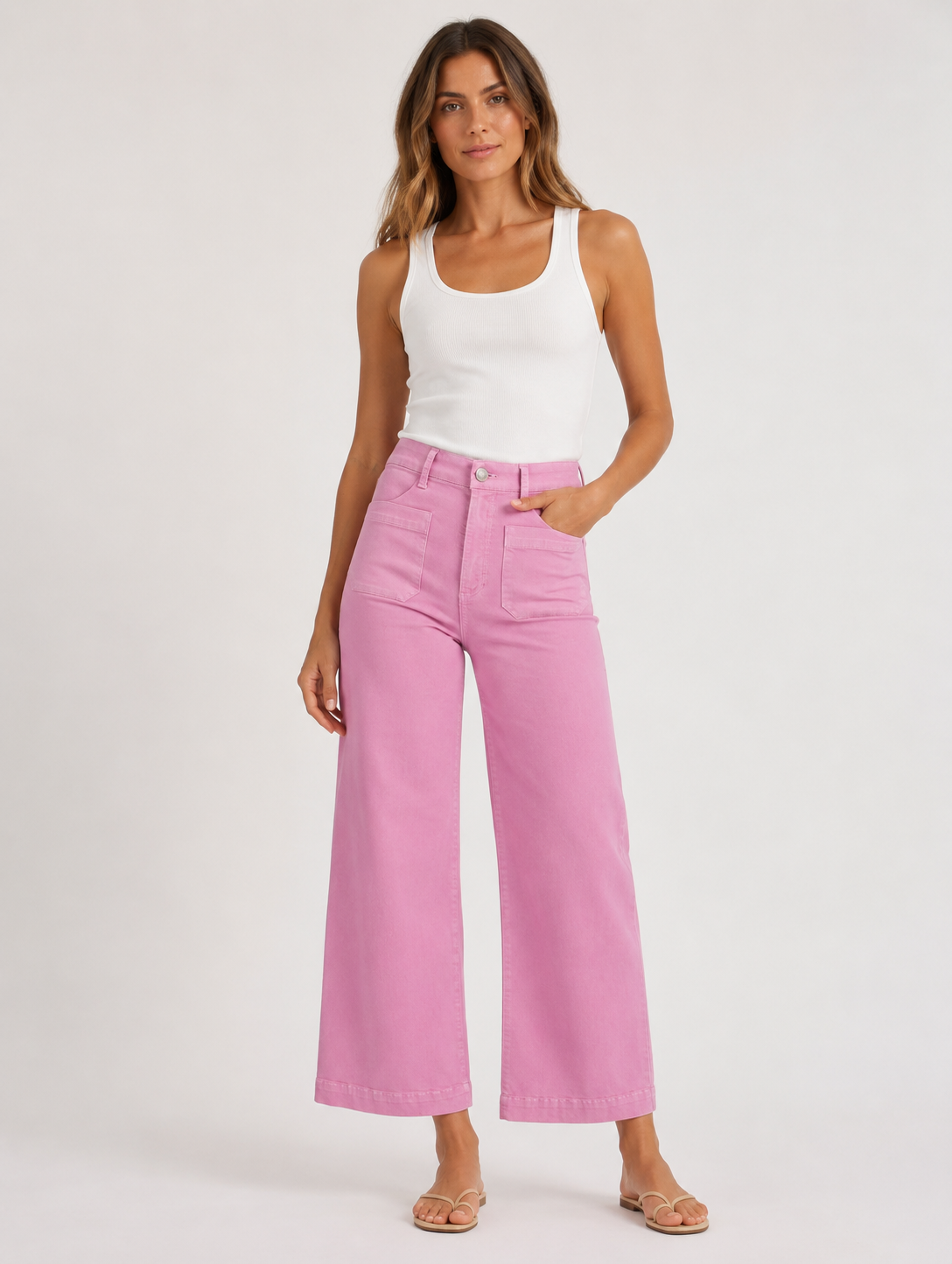 Woman wearing a white tank top and pink high-waisted pants on a white background