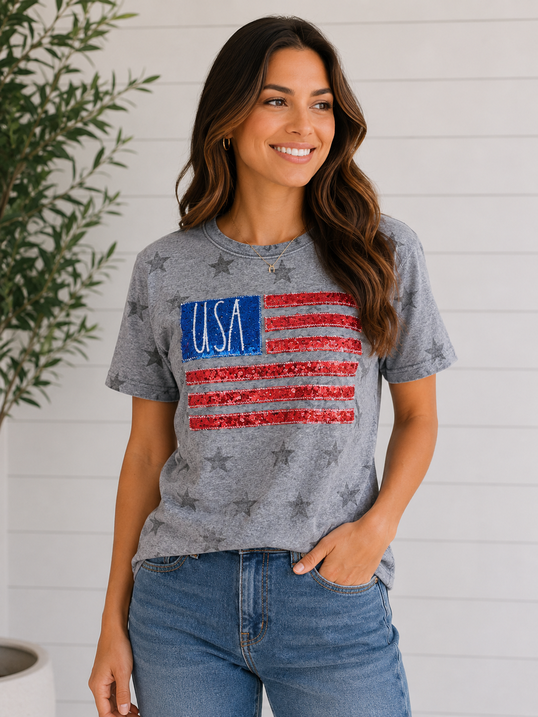 Woman wearing a gray t-shirt with USA flag design against a white wall.