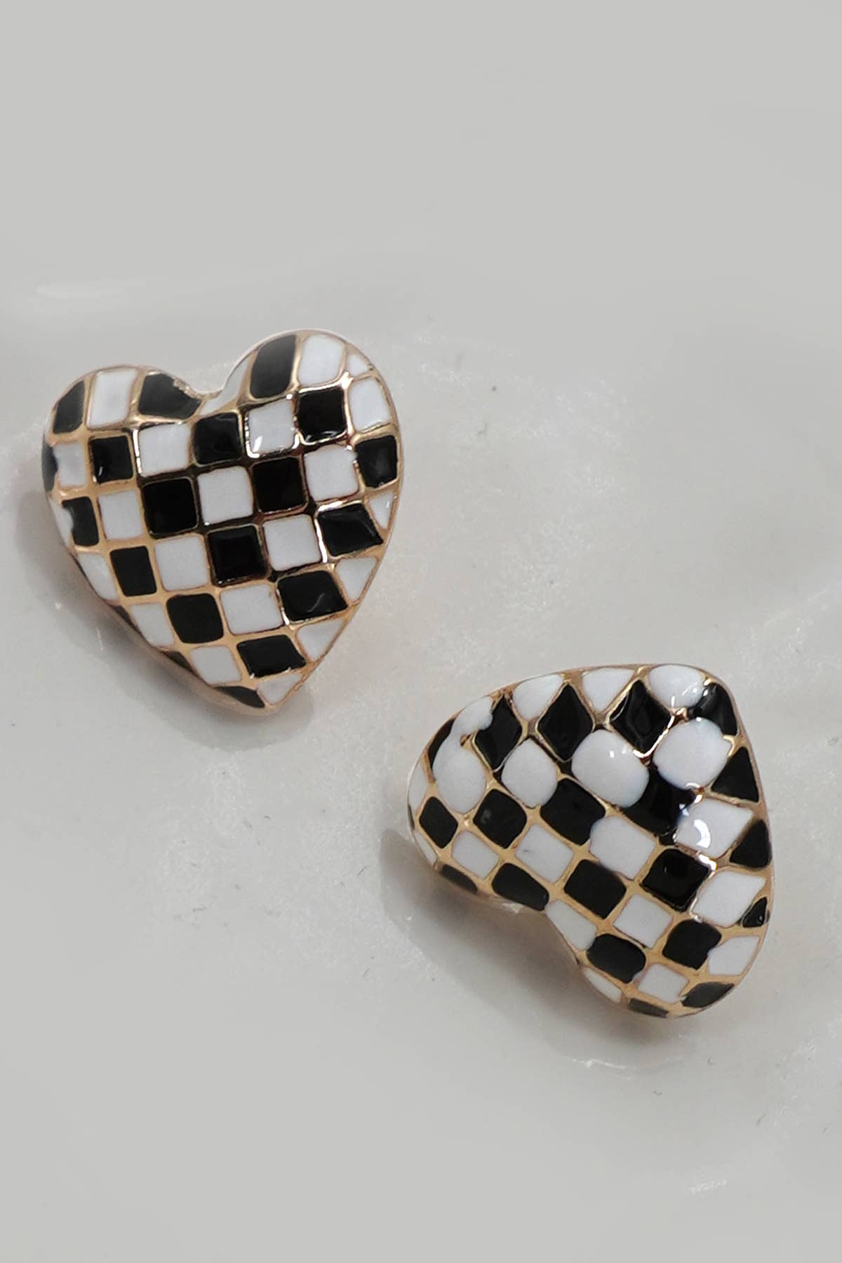 Heart-shaped earrings with black and white checkered pattern on a light gray background