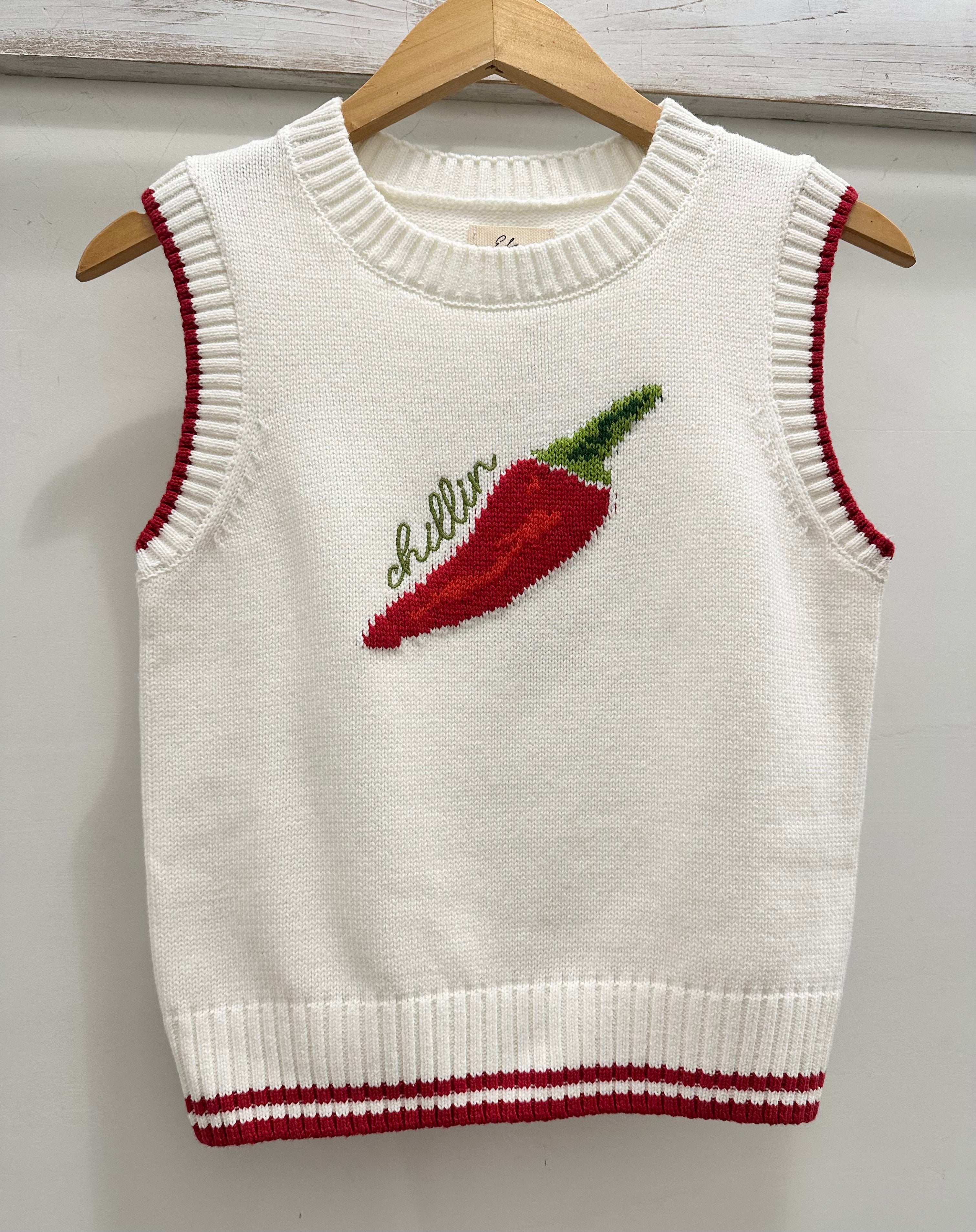 White knit sleeveless sweater with red chili pepper design and 'chillin' text on a wooden hanger.