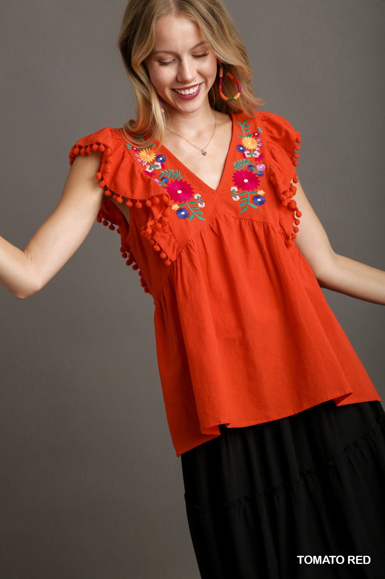 Woman wearing a tomato red blouse with floral embroidery on a gray background