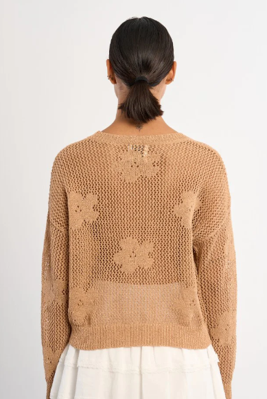 Person wearing a beige knitted sweater with floral patterns on a white background