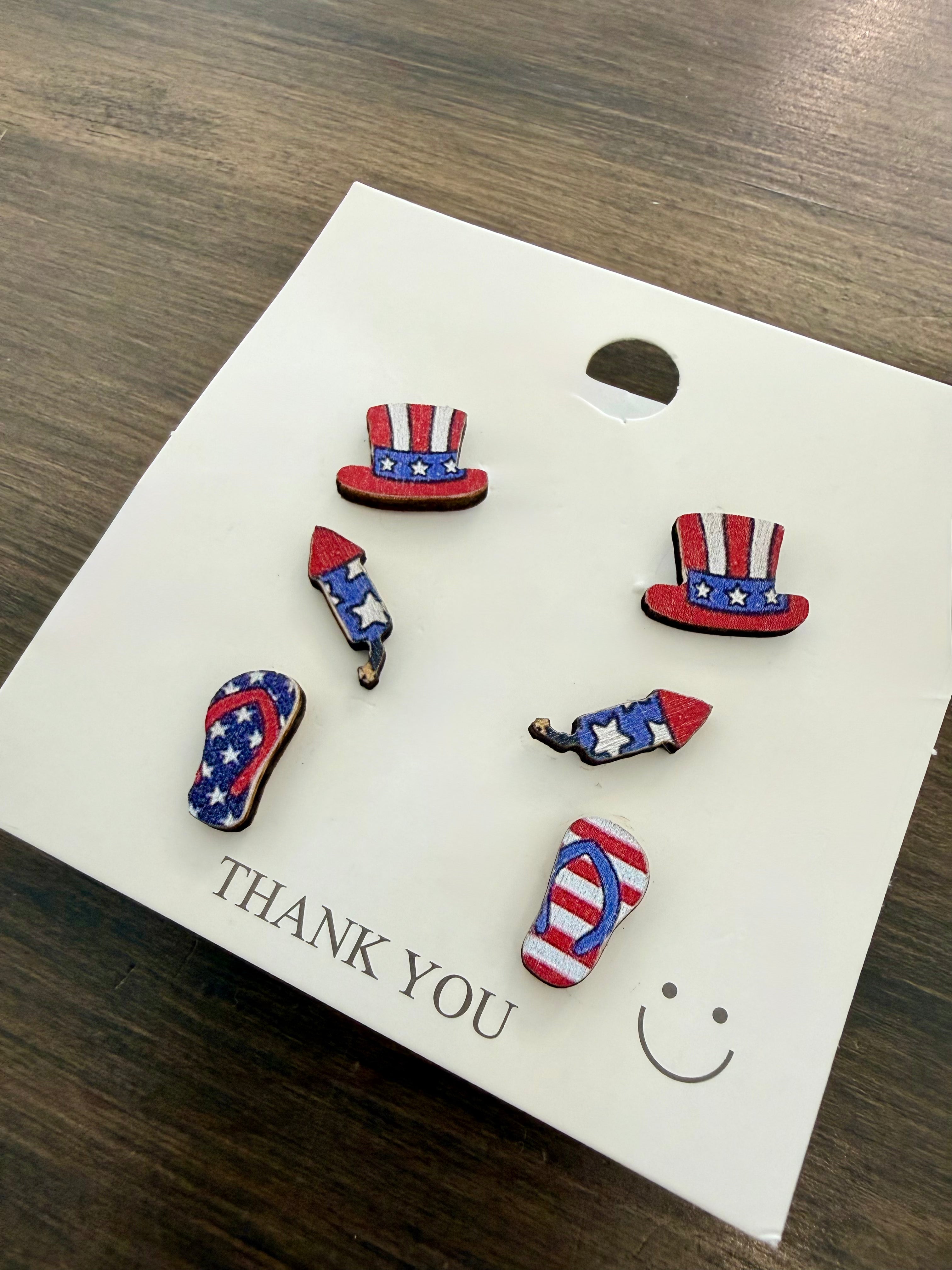 Set of patriotic earrings on a 'Thank You' card with a smiley face, displayed on a wooden surface.