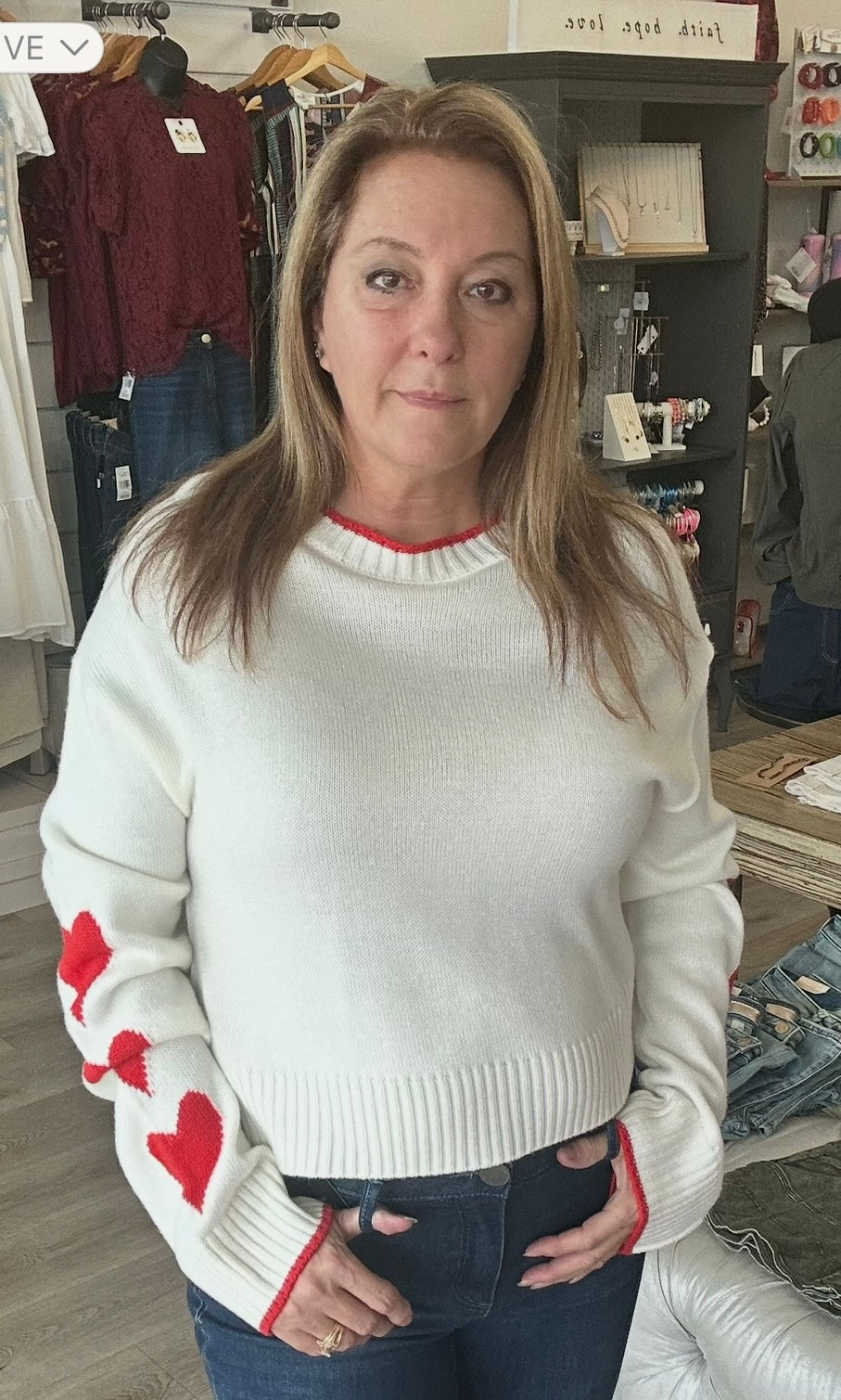 Woman wearing a white sweater with red heart patterns in a store setting