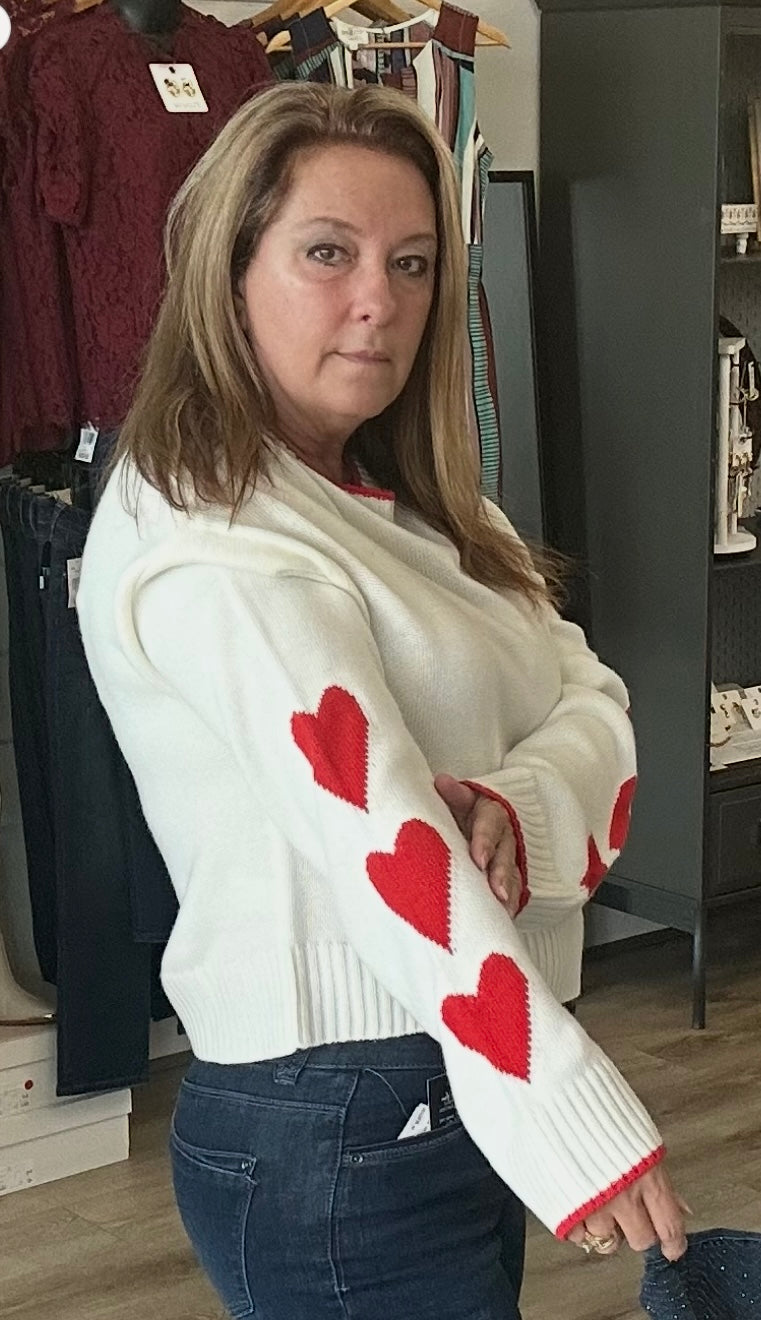 Woman wearing a white sweater with red heart patterns in a clothing store.