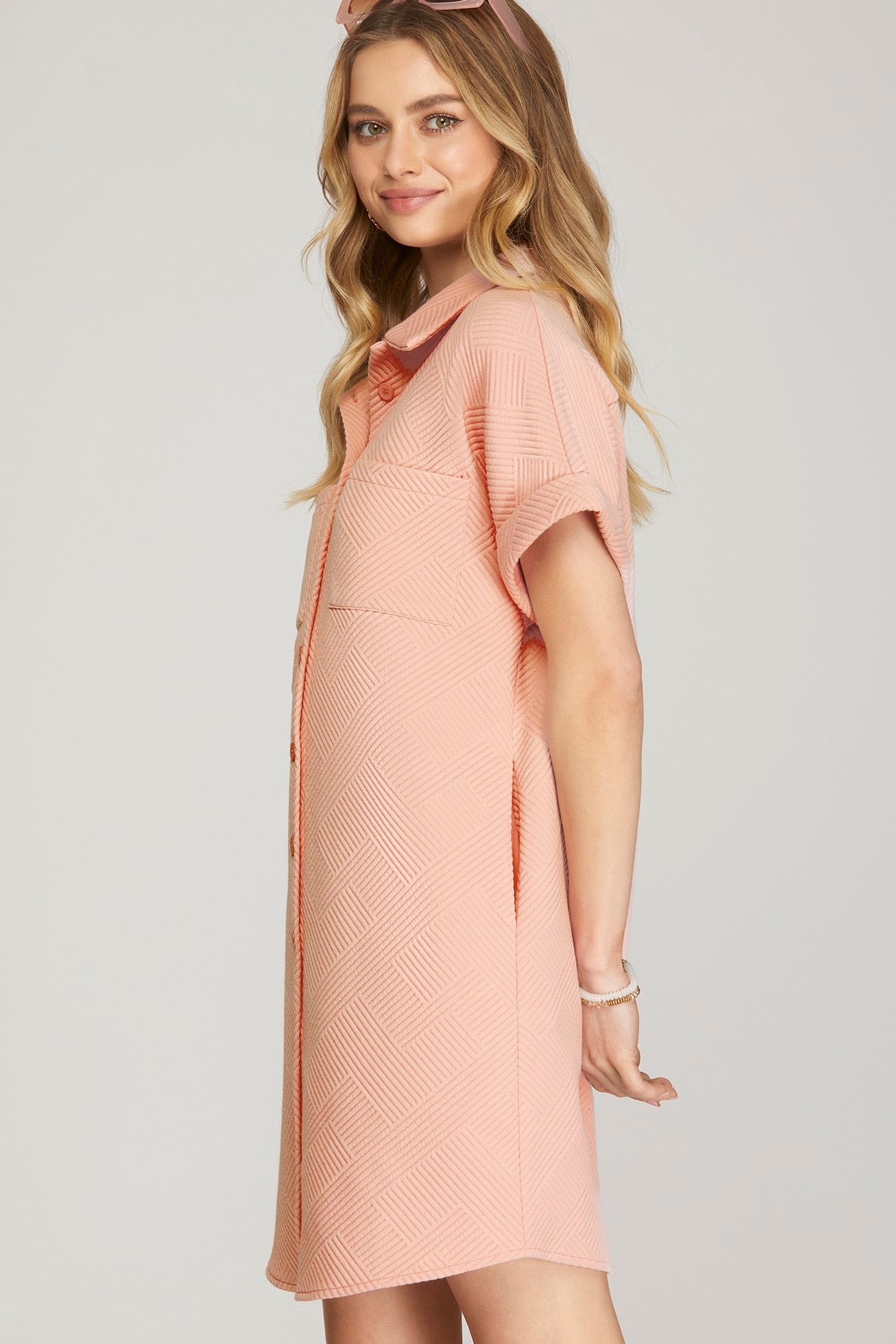 A woman wearing a short-sleeve, collared knit dress in a soft peach-pink color, photographed against a light gray studio background.