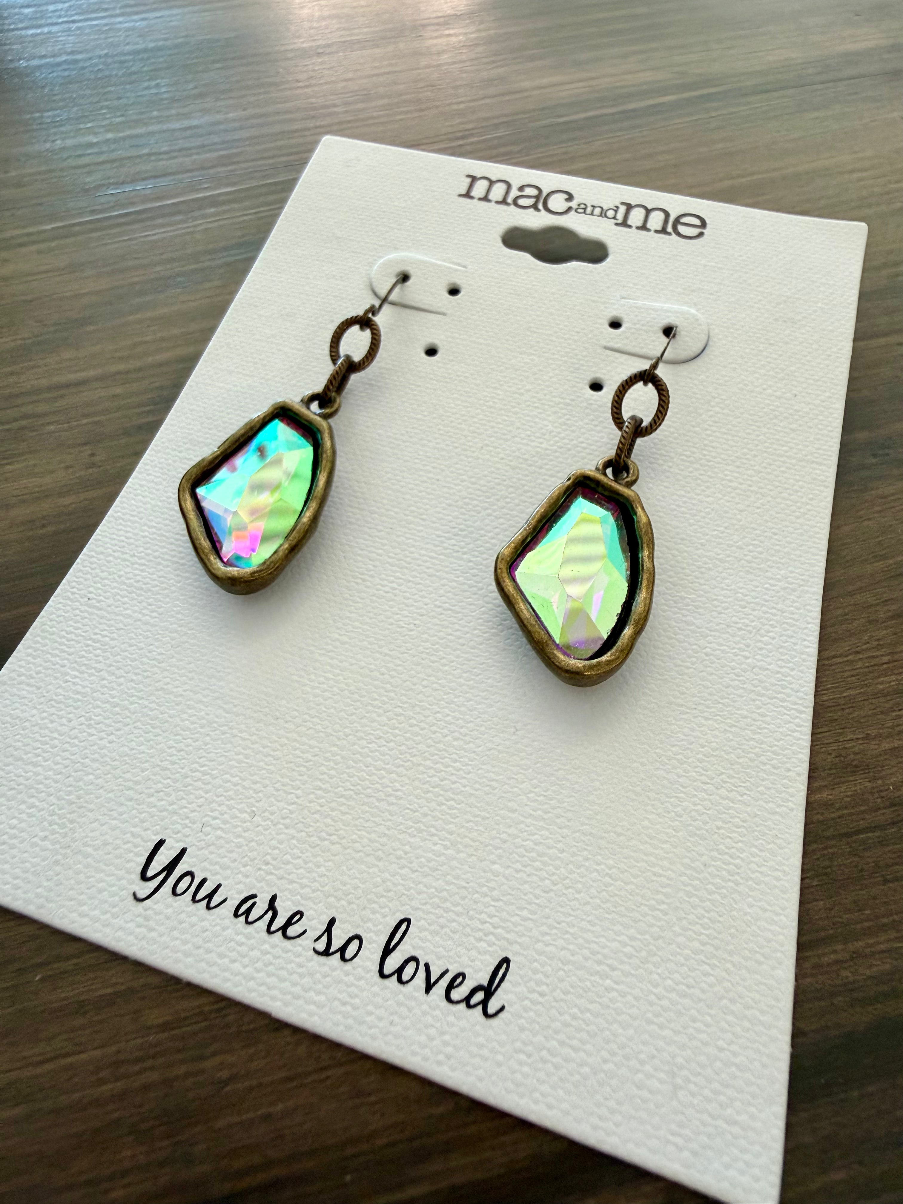 Pair of earrings on a 'mac & me' branded card with a message on a wooden surface.