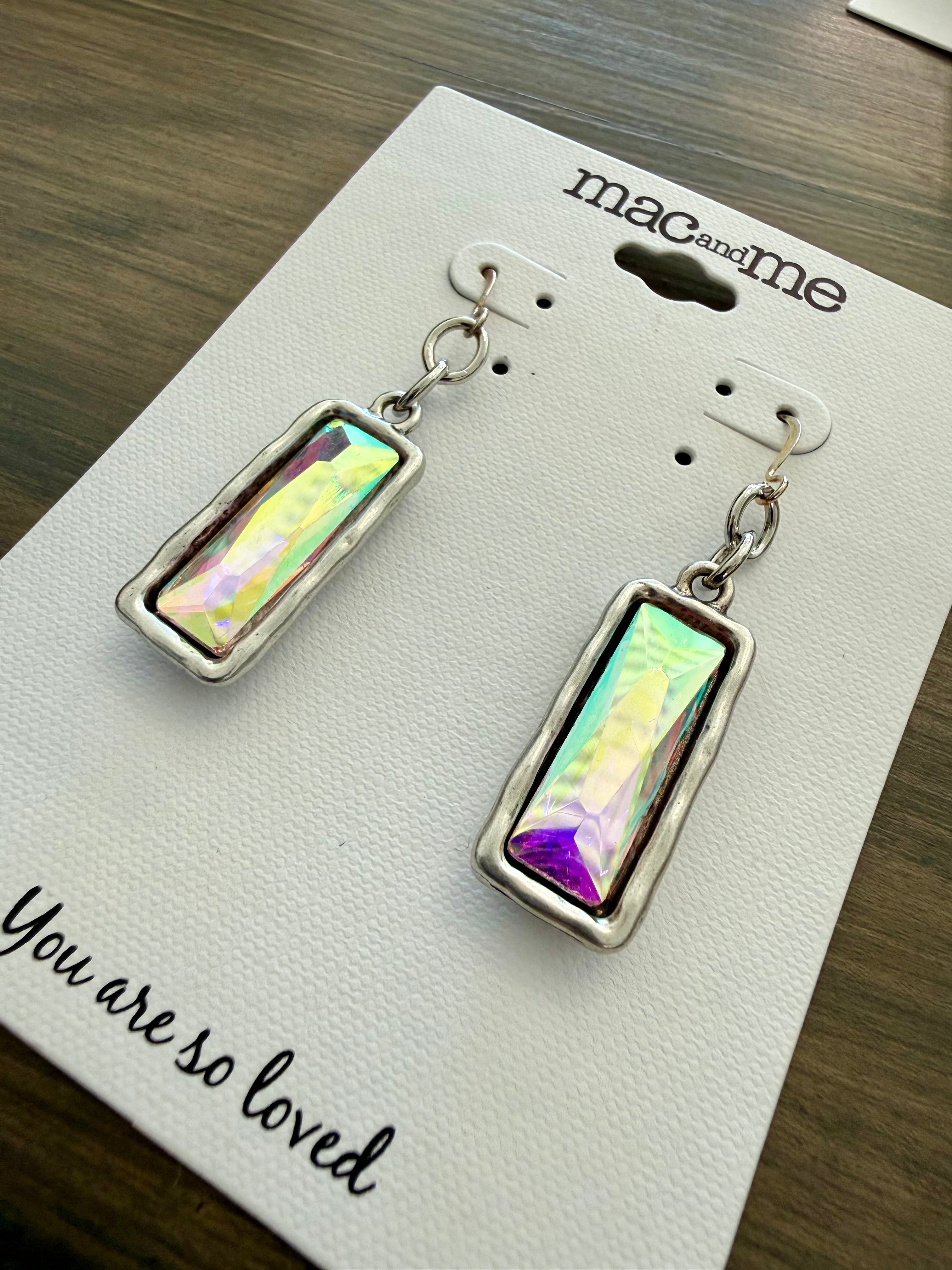 Pair of earrings on a 'mac and me' branded card with a message on a wooden surface.