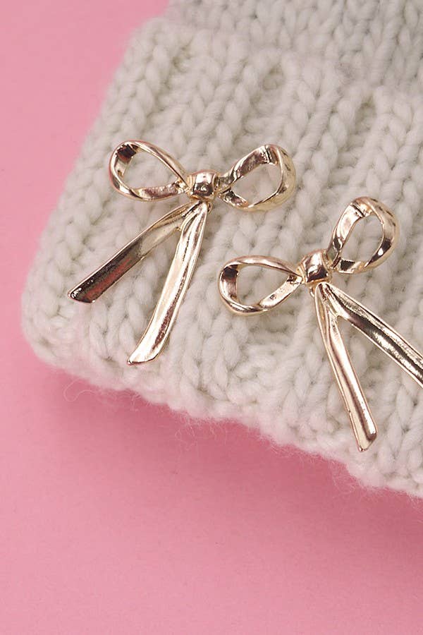 Gold bow-shaped earrings on a textured surface with pink background