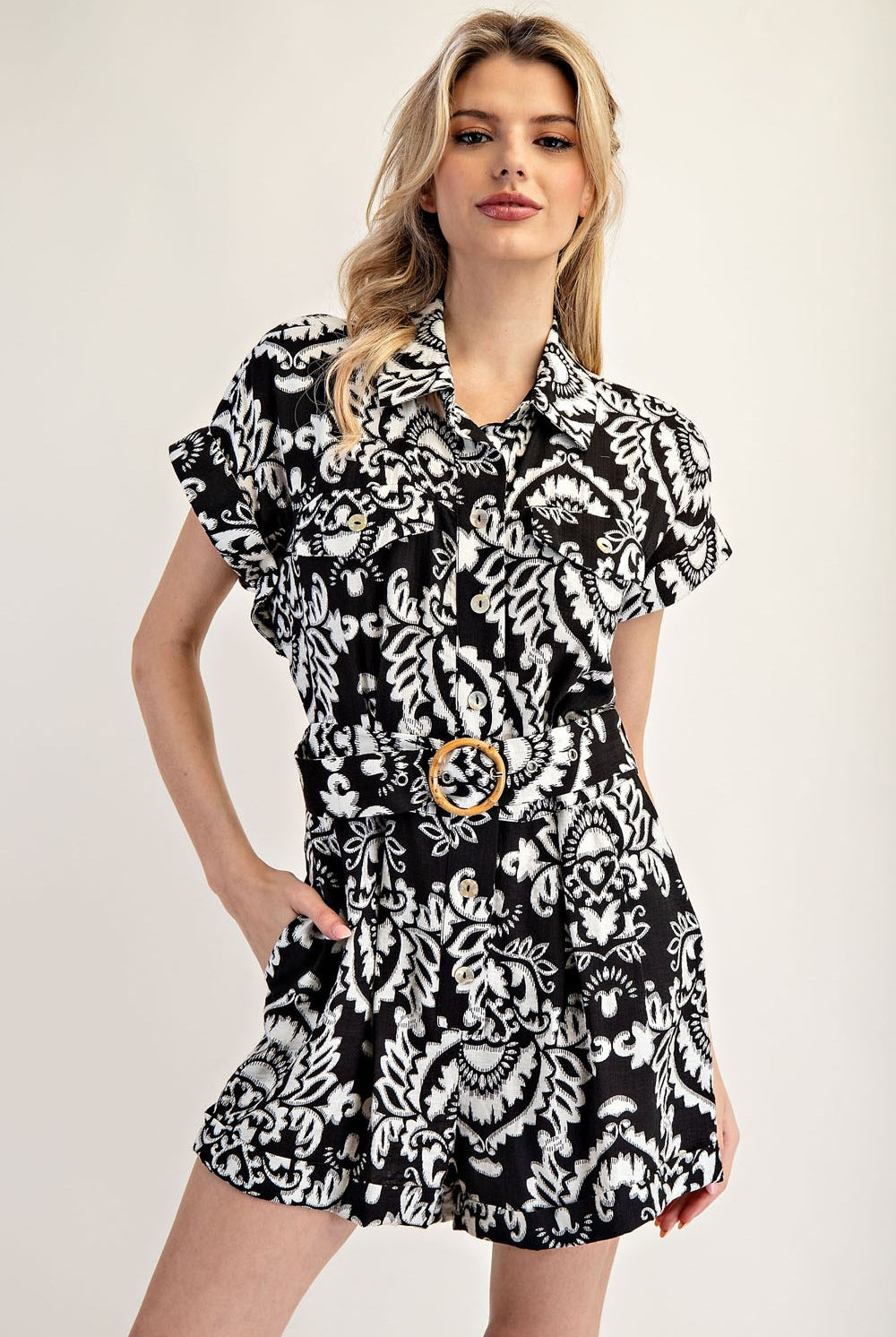 Woman wearing a black and white patterned dress with a belt on a plain background