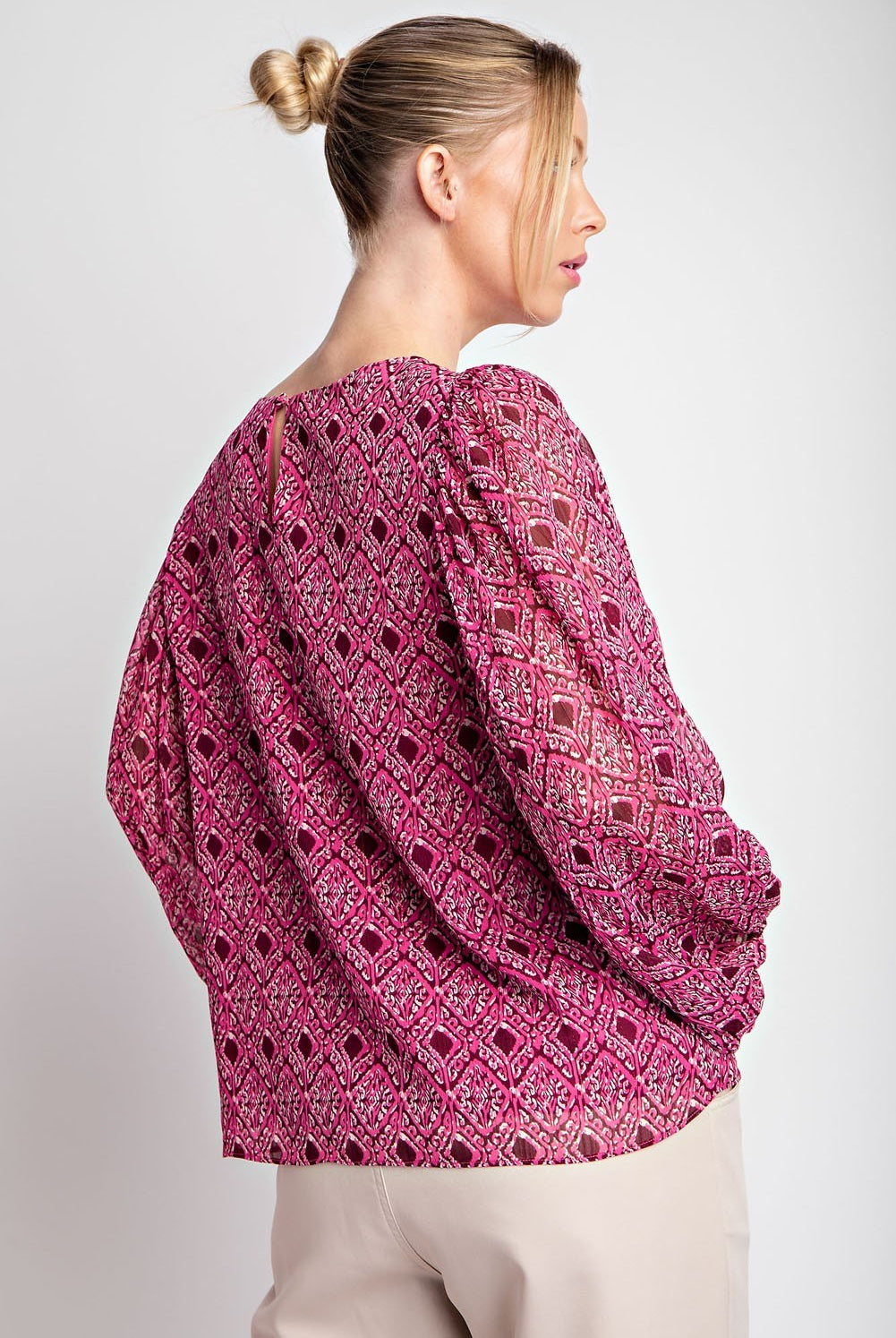 Woman wearing a pink patterned blouse against a plain background