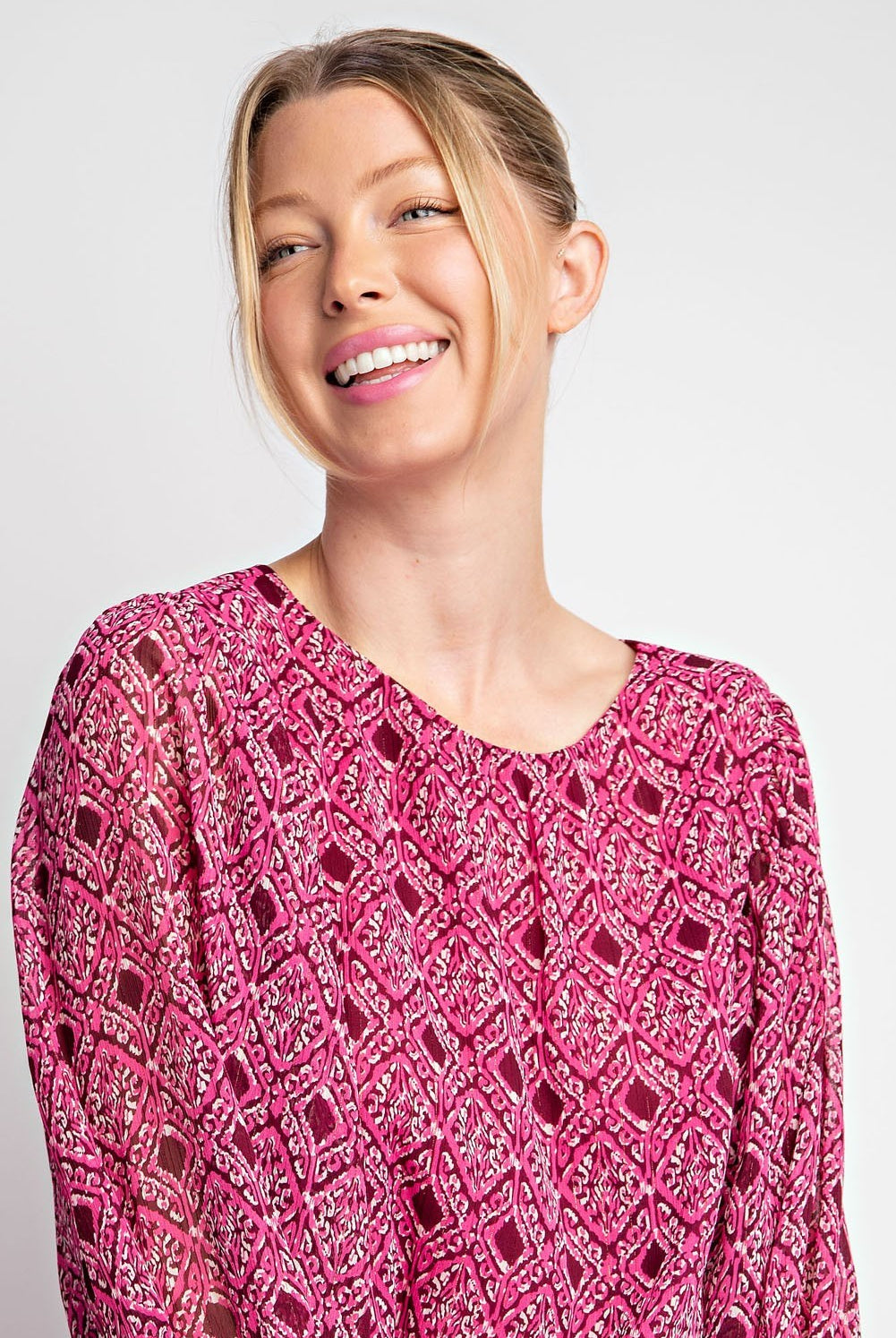 Woman wearing a pink patterned top against a plain background