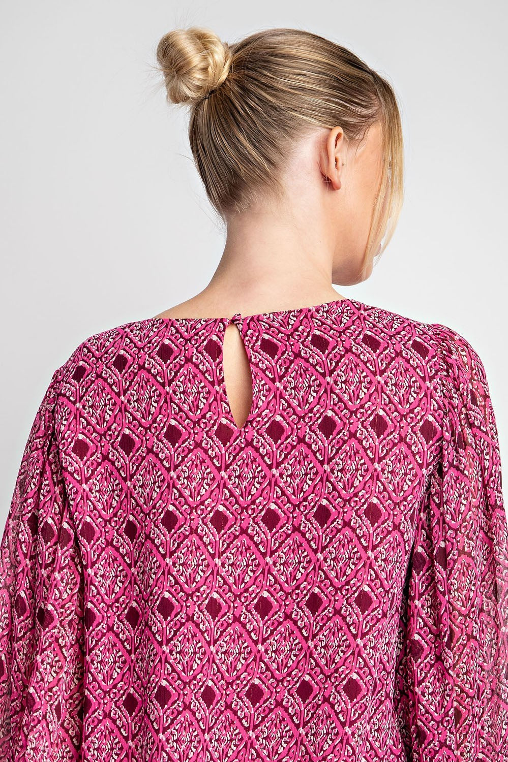 Pink patterned blouse worn by a person with a plain background
