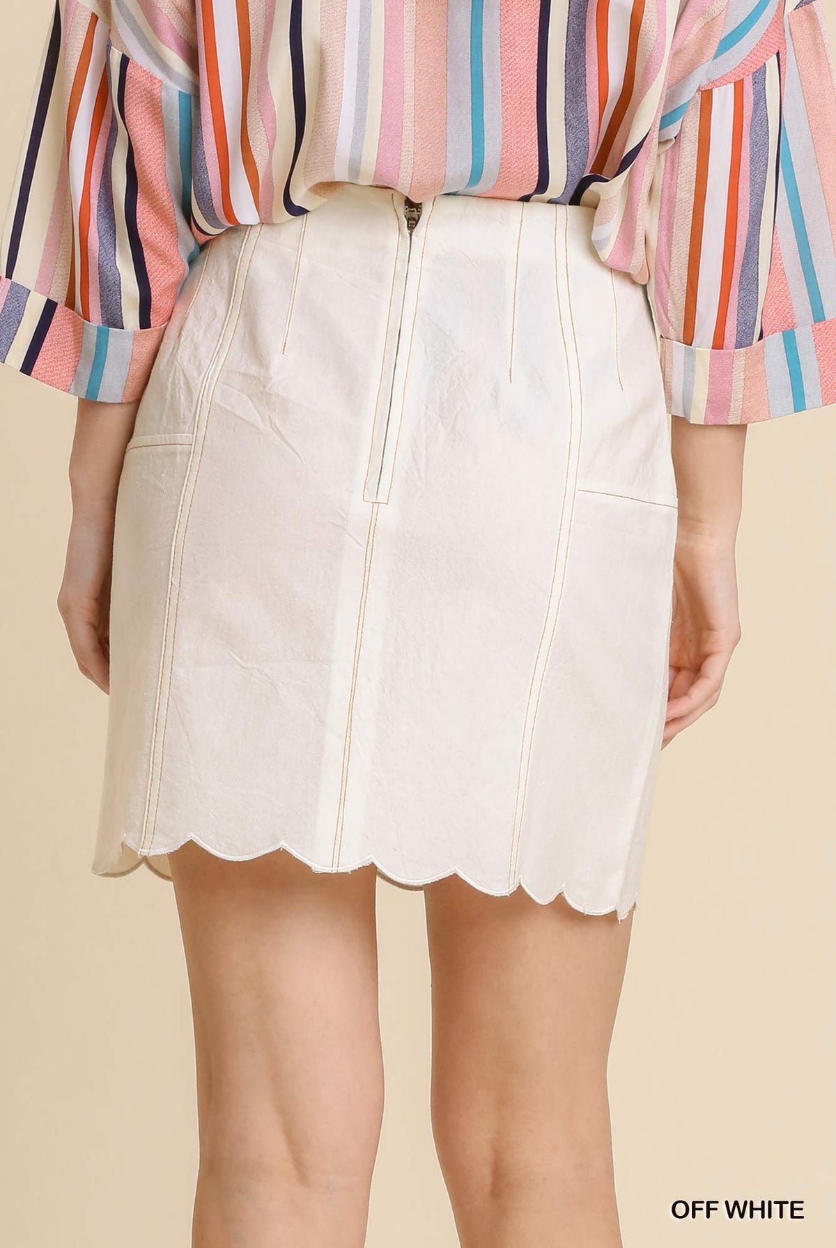 Person wearing a striped shirt and off-white skirt on a beige background