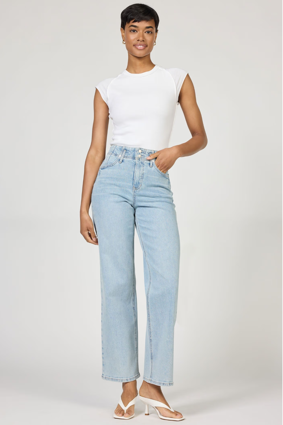Woman wearing light blue jeans and a white top on a plain background