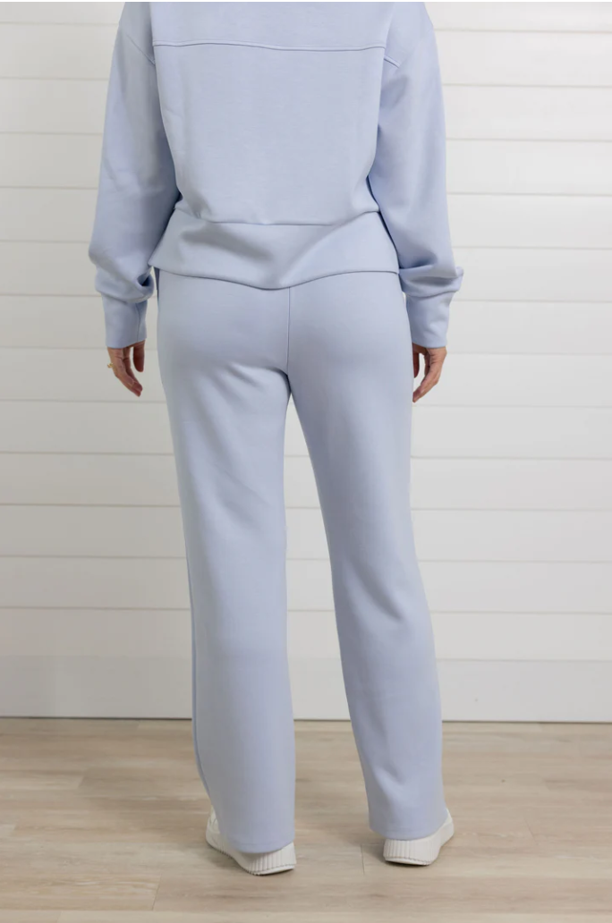 Light blue tracksuit worn by a person on a wooden floor with white wall background