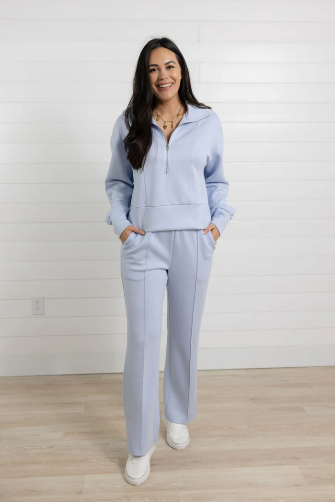 Woman wearing a light blue tracksuit standing in a room with a white wall and wooden floor.