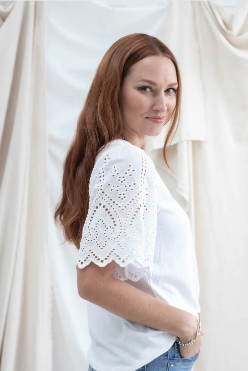 Woman wearing a white blouse with lace details against a white curtain background