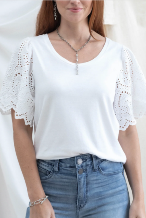 Woman wearing a white blouse with lace details and blue jeans against a plain background