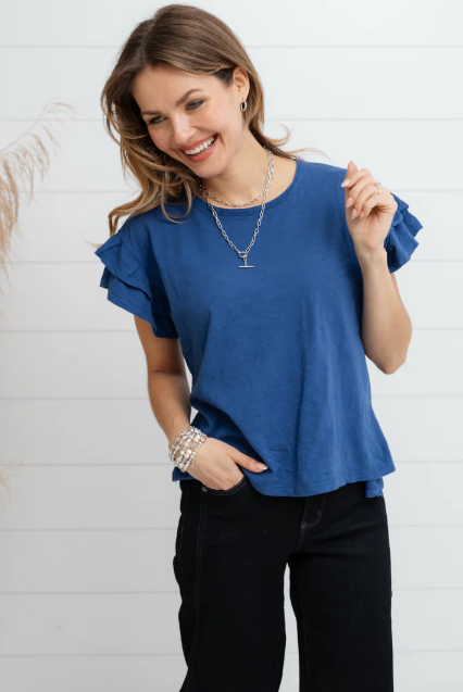Woman wearing a blue ruffled blouse and black pants against a white background
