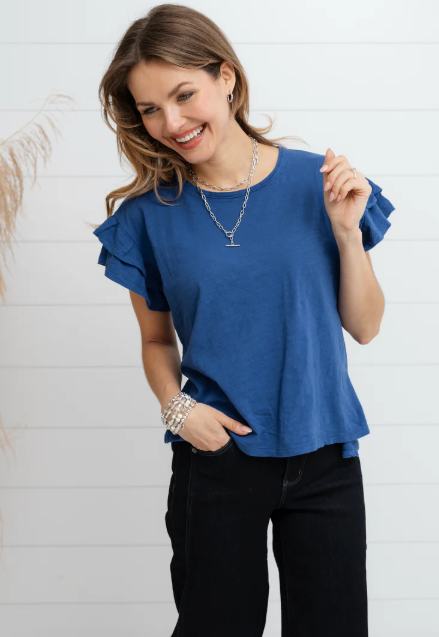 Woman wearing a blue ruffled blouse and black pants against a white background