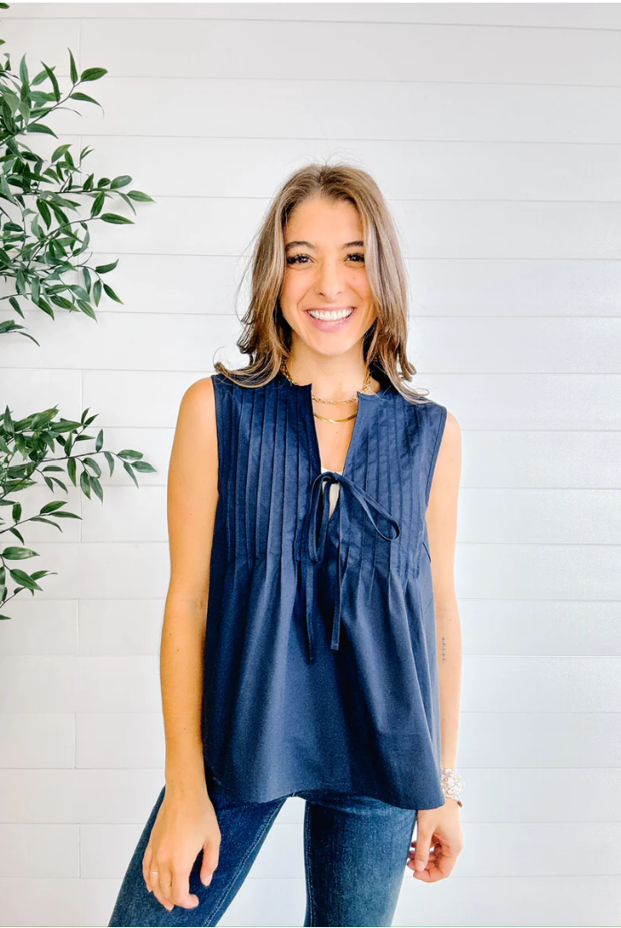 Woman wearing a navy sleeveless top with a white background and green plant.