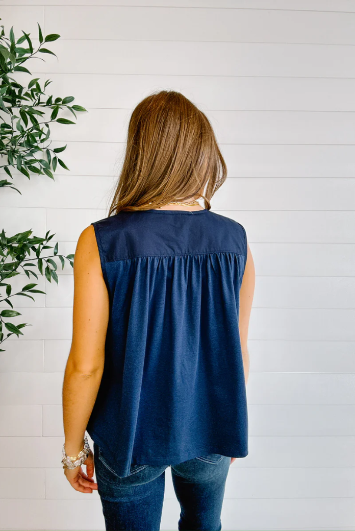 Woman wearing a navy sleeveless top against a white wooden panel background