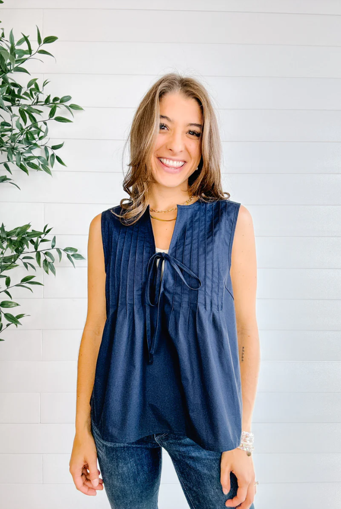 Woman wearing a sleeveless blue top with a white background and green plant