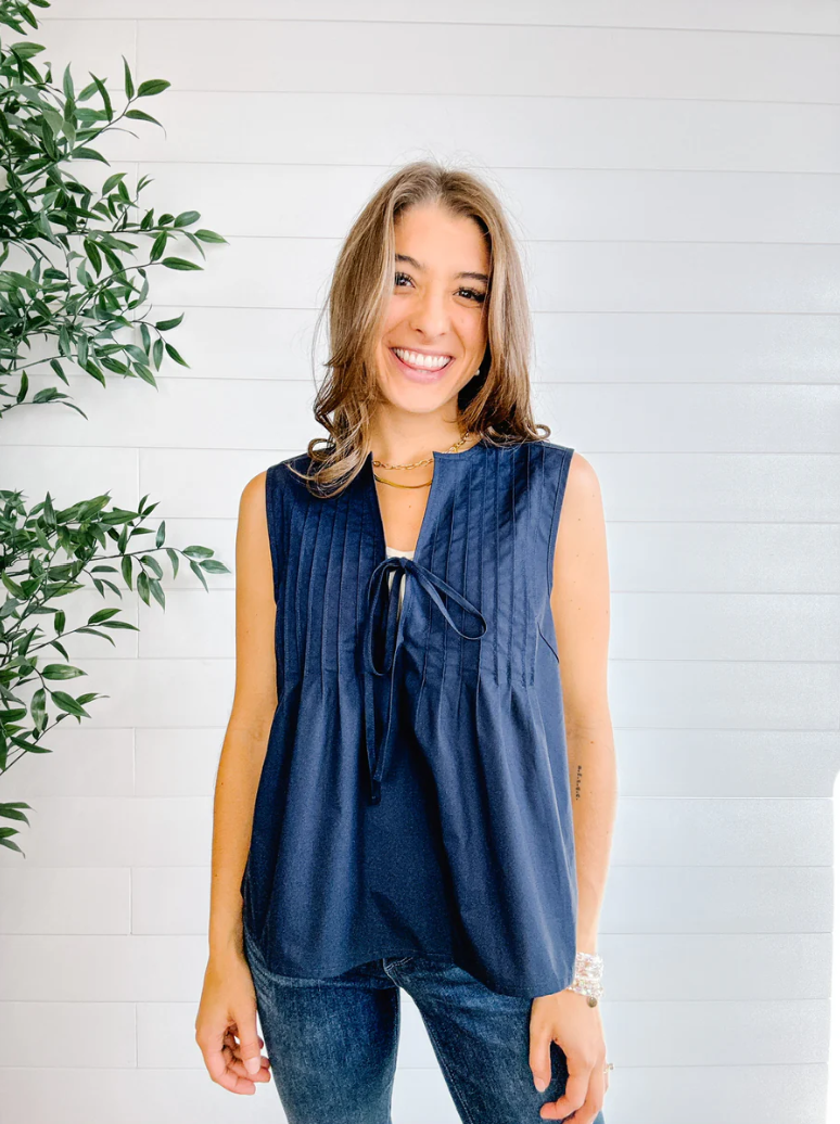 Woman wearing a sleeveless blue top with a white background and green plant