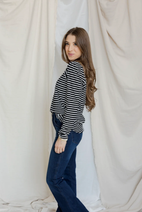 Woman wearing a striped shirt and jeans standing against a white curtain