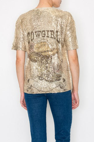 Person wearing a gold sequin 'COWGIRL' top and blue jeans on a white background