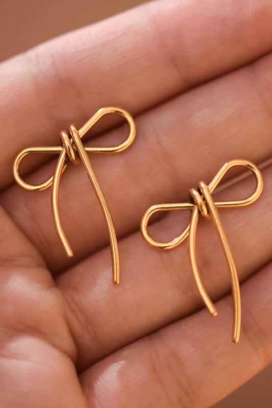 Gold bow-shaped earrings held in a hand against a brown background
