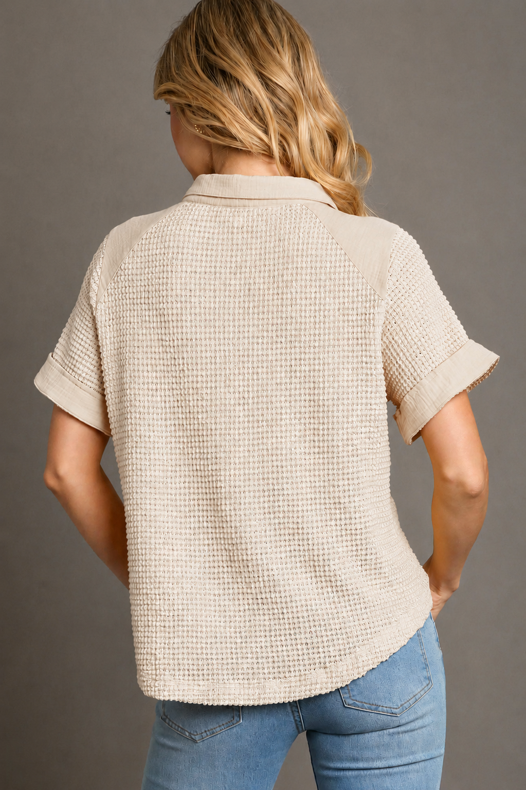 Woman wearing a beige textured shirt and blue jeans against a gray background