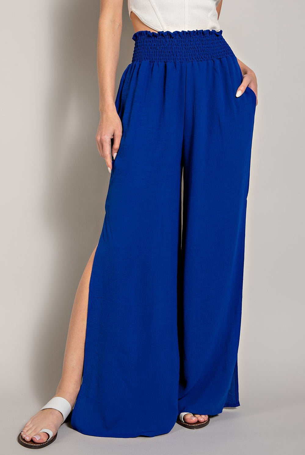 Person wearing blue wide-leg pants with a white top on a plain background