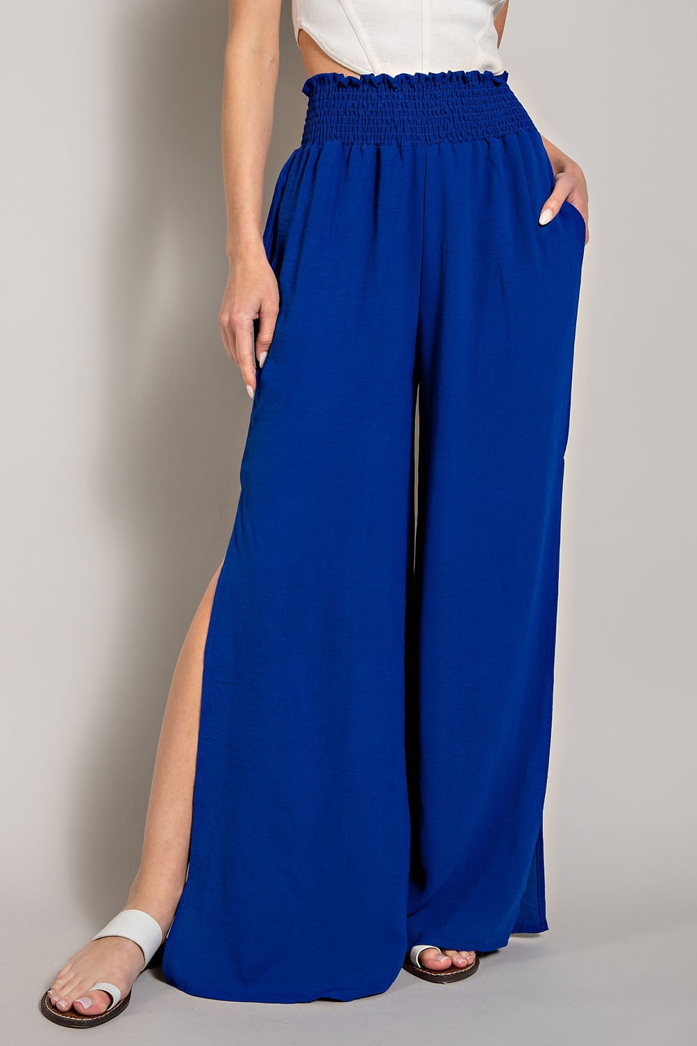 Person wearing blue wide-leg pants with a white top on a plain background