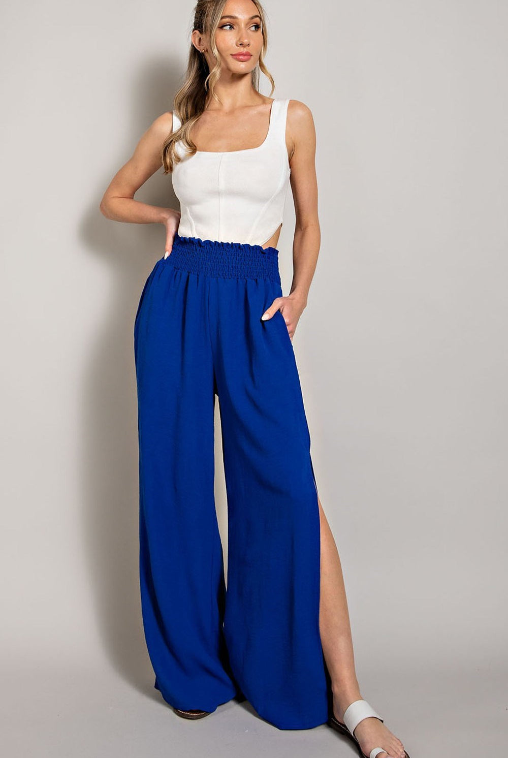 Woman wearing a white top and blue wide-leg pants on a plain background