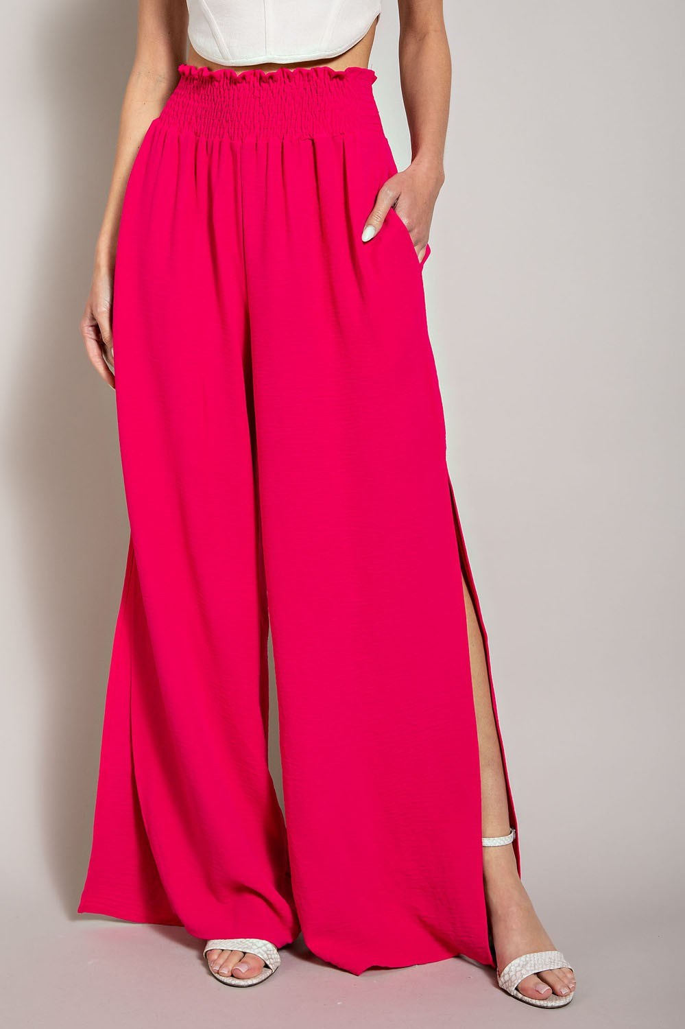 Person wearing bright pink wide-leg pants with a white top on a plain background
